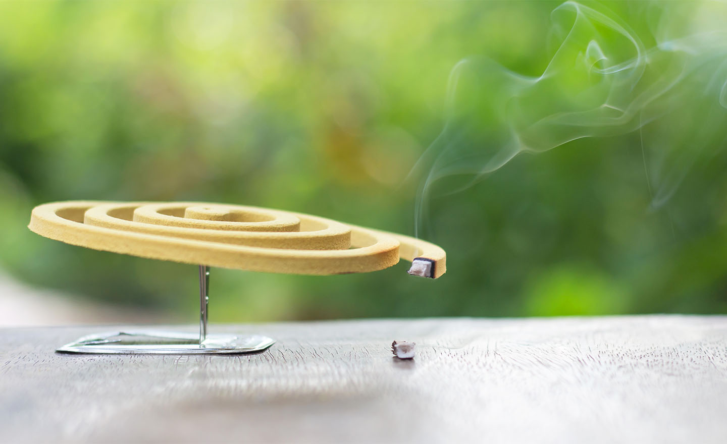Yellow mosquito repellent and white smoke on wooden table with green blur light space background for text.