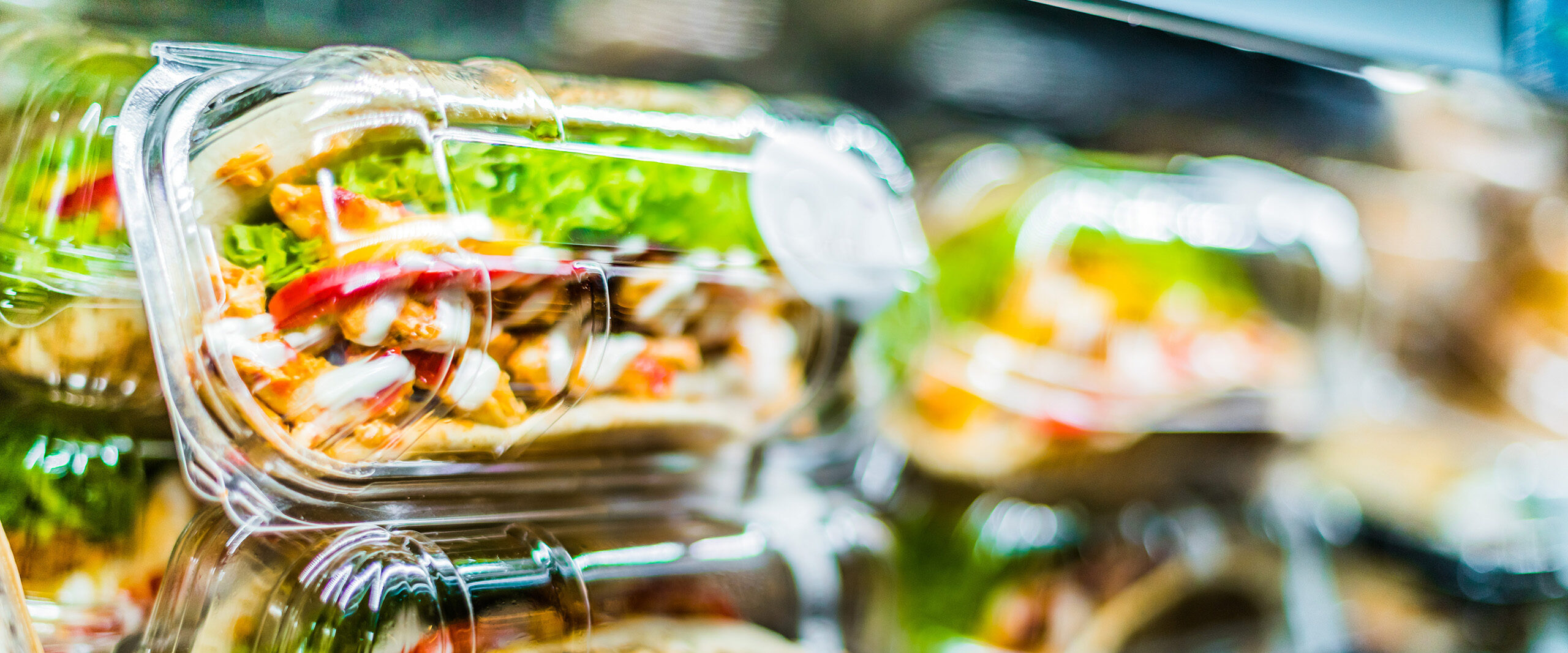Glass food containers with layered salad on a conveyor belt in a restaurant setting.