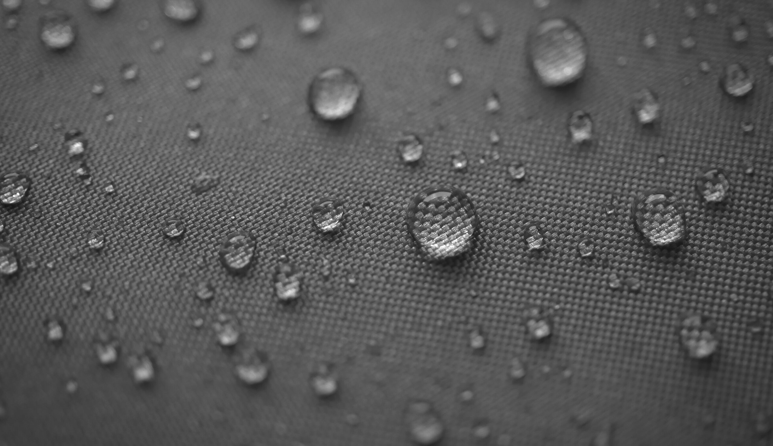 Macro shot of water droplets beading on dark fabric textile.