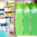 Row of bright green detergent bottles aligned on a store shelf with blurred background shelves behind them.