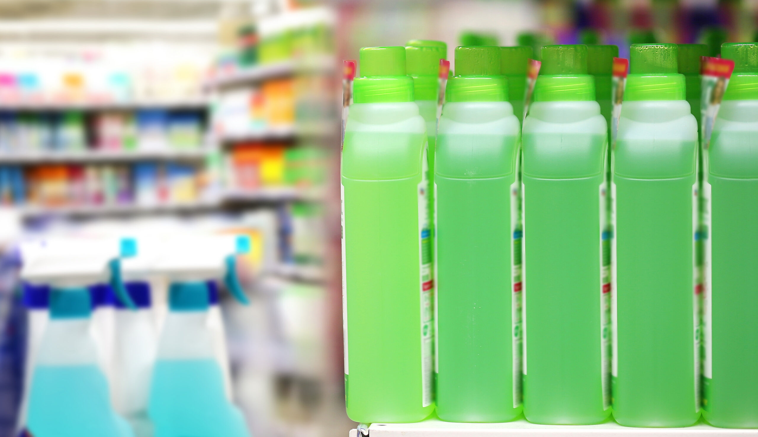 Row of bright green detergent bottles aligned on a store shelf with blurred background shelves behind them.