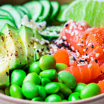 Close-up of a colorful poke bowl with sliced avocado, salmon, edamame, cucumber, and sesame seeds in a wooden bowl