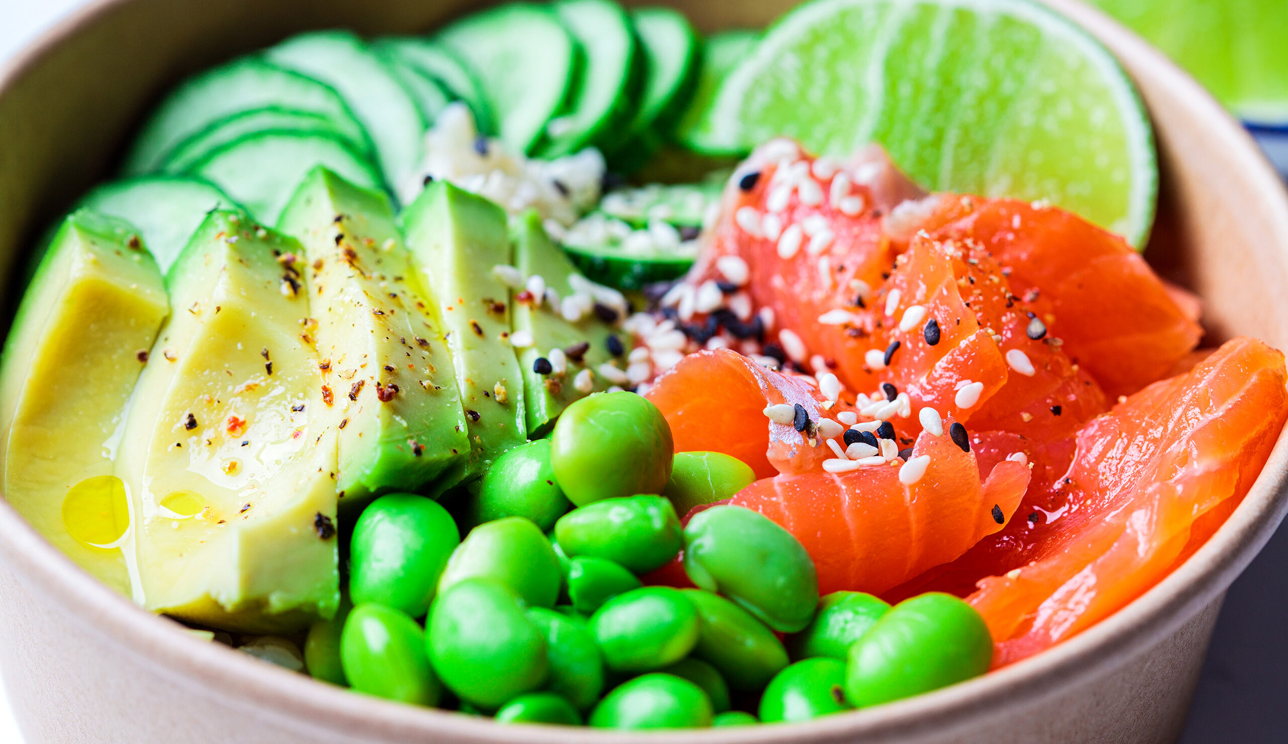 Close-up of a colorful poke bowl with sliced avocado, salmon, edamame, cucumber, and sesame seeds in a wooden bowl