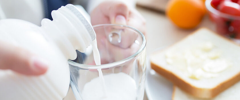 Pouring milk into a glass at a breakfast setup with buttered toast in the background.