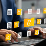 Hands typing on a laptop with floating yellow-and-white security document icons around the keyboard.