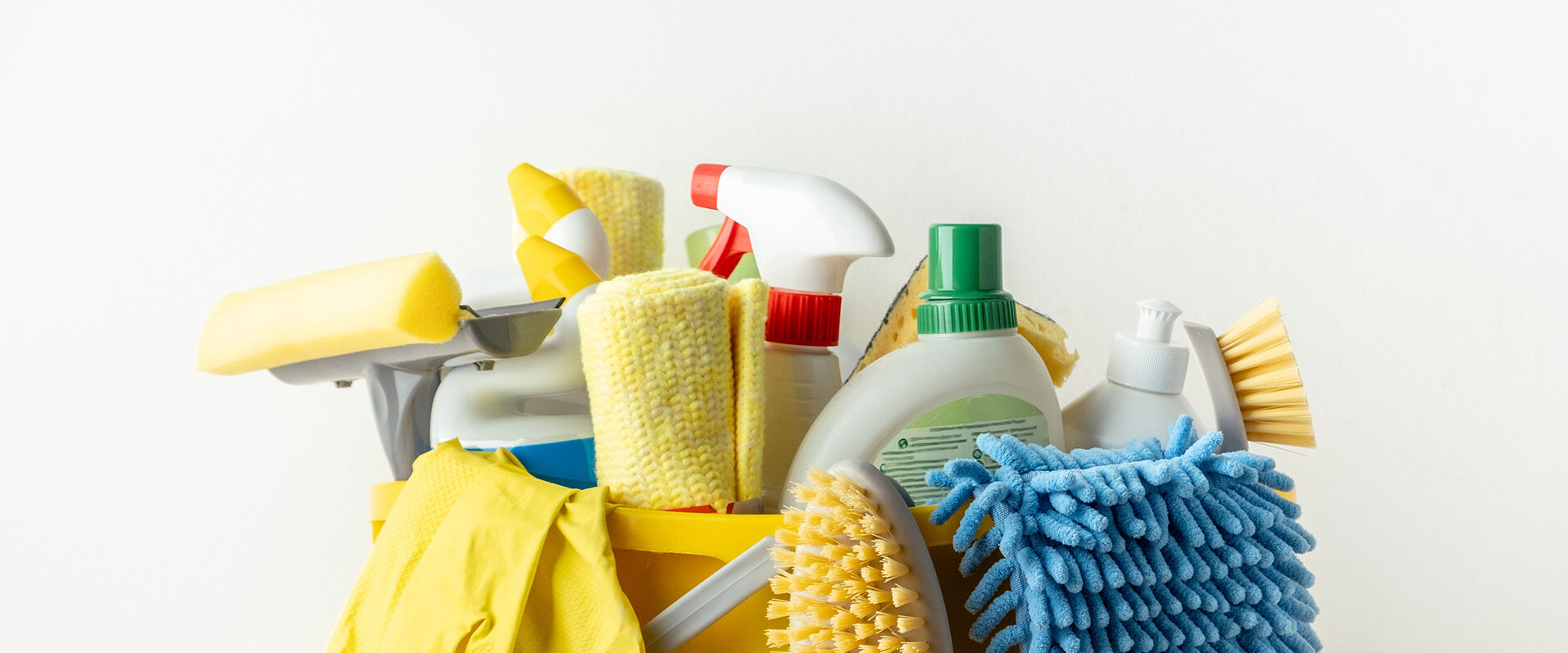 Assorted cleaning supplies in a yellow bucket, including sponges, spray bottle, brushes, and gloves.