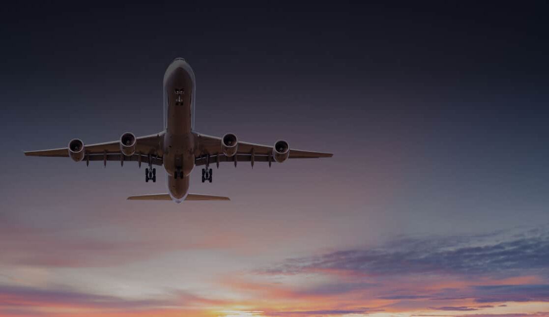 Low-angle view of a commercial airliner approaching for landing with landing gear down against a sunset sky.