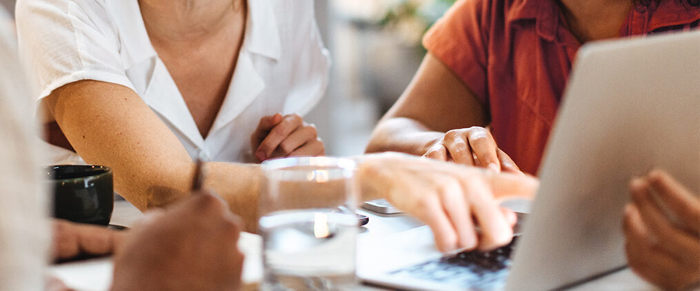 Team members collaborate around a laptop, discussing documents at a bright table.