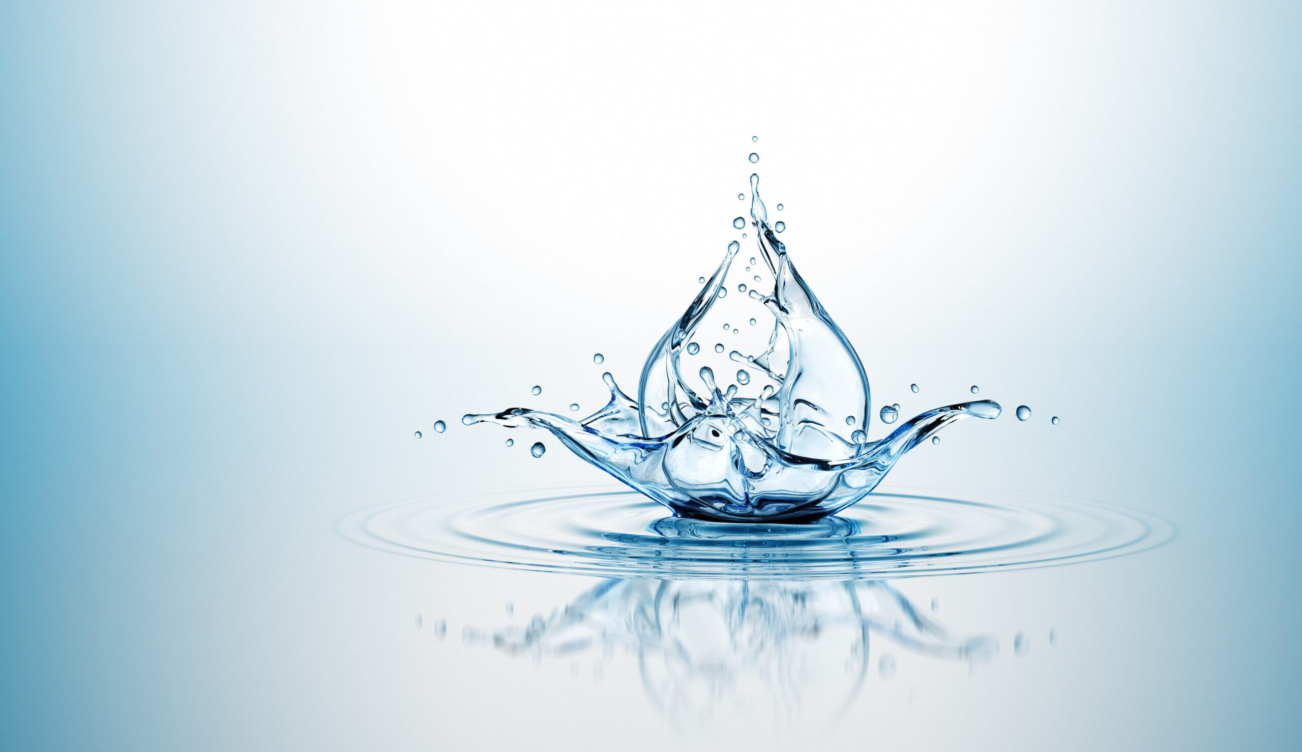 High-speed shot of a blue water splash forming a crown shape with droplets in mid-air against a pale blue gradient background, reflecting on the water surface.