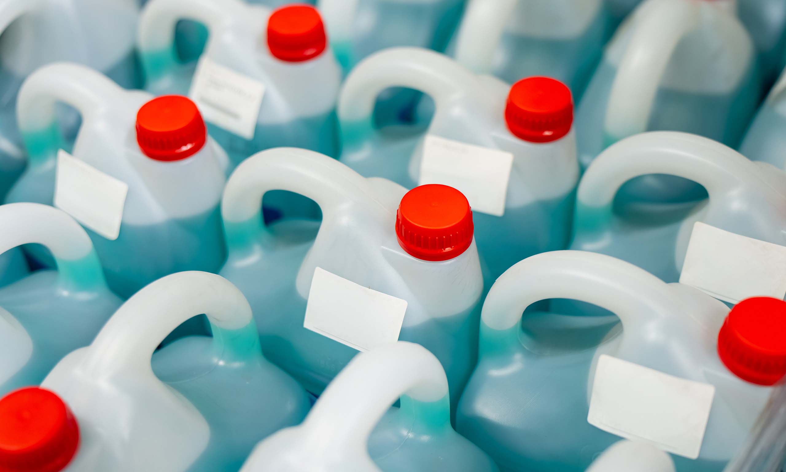 Close-up of white plastic containers with red screw caps and blank labels, packed together in a crowd of jugs.