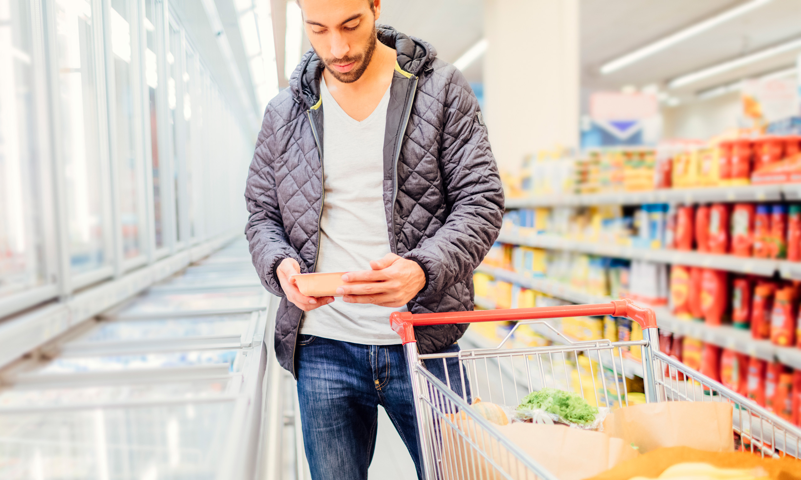 Young man looking at label in frozen food aisle of supermarket representing Leatherhead Food Research's cooking instructions services