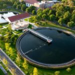Aerial view of a circular wastewater treatment tank with a red-roof pavilion and surrounding green park area.